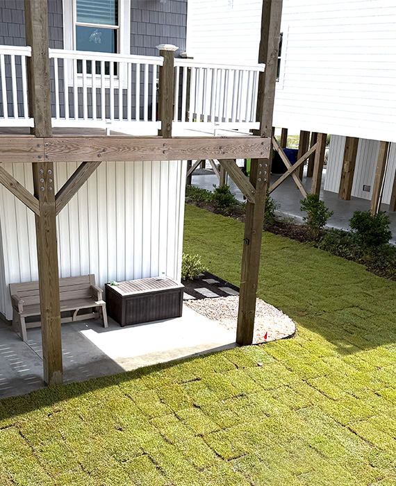 Foundation landscaping with newly installed sod, decorative stone, evergreen shrubs, and landscape edging surrounding an elevated home.