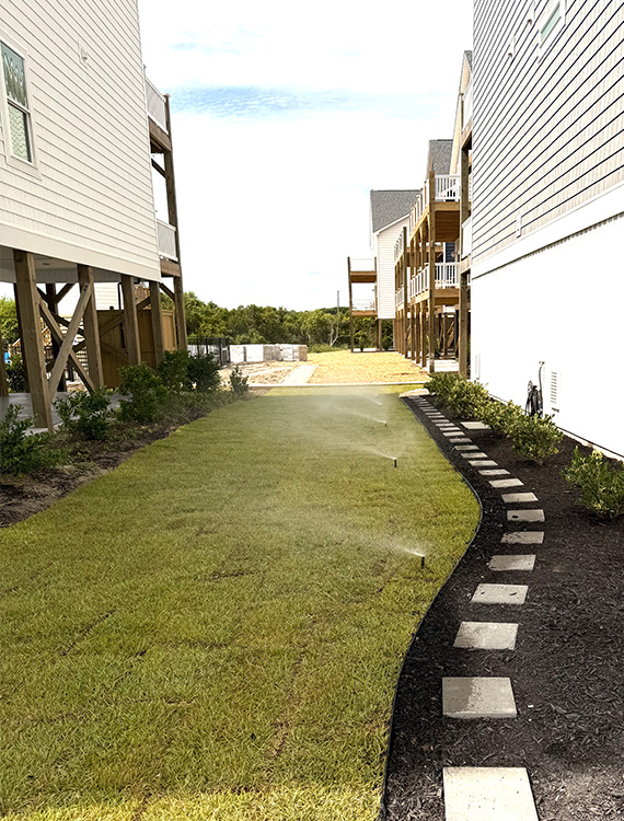 Newly installed lawn with irrigation sprinklers, foundation shrubs, mulch beds, and stepping stones designed for healthy turf growth.