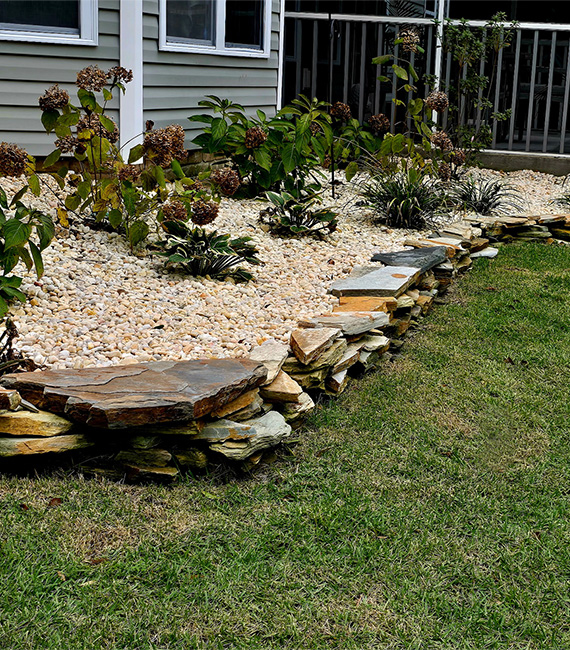 Natural stone landscape border with decorative river rock, perennial plantings, and layered garden beds creating a polished residential landscape.