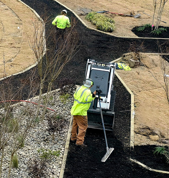 Landscape crew installing fresh mulch and finishing landscape beds with compact equipment as part of a commercial property improvement project.
