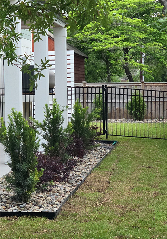 Decorative river rock landscape with evergreen shrubs, colorful foliage, and clean edging creating a polished foundation planting around a home.