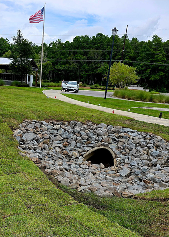 Stormwater drainage system with riprap stone around a culvert to improve water flow and reduce erosion on a commercial property.