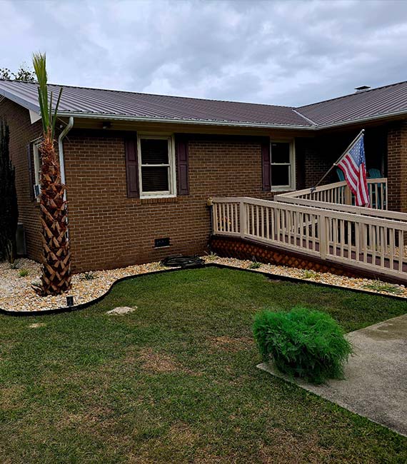 Front yard landscape renovation featuring a newly planted palm tree, decorative stone beds, crisp landscape edging, and a healthy lawn.